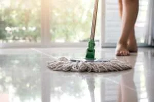 Glanzende keramische vloertegels schoonmaken met dweil in een moderne woonkamer met grote ramen.