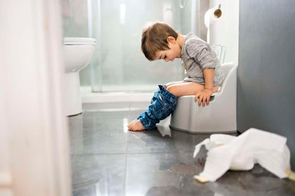 Peuter zindelijk maken op het potje op glanzende badkamertegels met toilet op de achtergrond.
