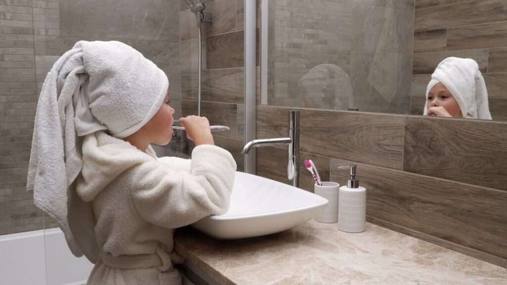 Kind poetst tanden in moderne badkamer met houtlook wandtegels en marmer wastafel, voor een warme en luxe uitstraling.
