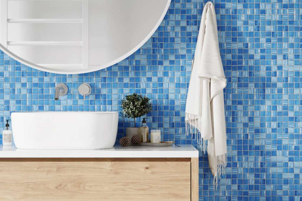 Moderne badkamer met blauwe mozaïektegels, houten wastafelmeubel, witte waskom, ronde spiegel en stijlvolle accessoires – inspiratie voor een frisse en trendy badkamerinrichting.