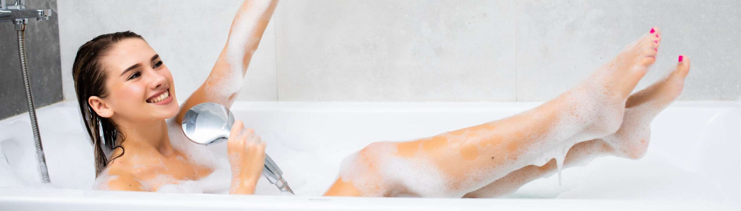 Lachende jonge vrouw geniet van een schuimbad in een moderne badkamer met badkuip en douche, ontspanning en wellness thuis.