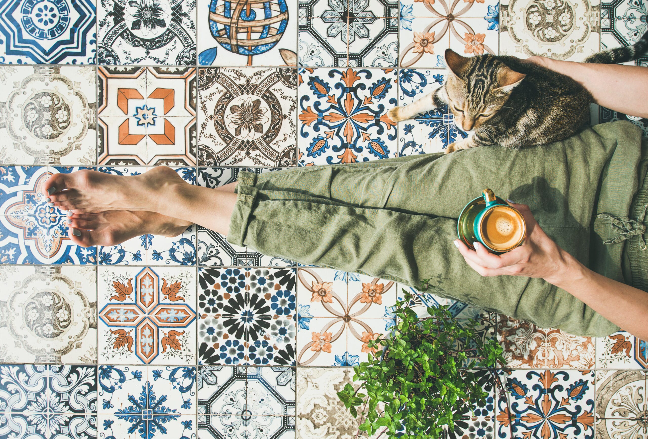 Vrouw ontspant met een kopje koffie en kat op een vloer van kleurrijke Portugese patroontegels; inspiratie voor Portugese tegels in huis, vintage look tegelvloer en decoratie-ideeën met keramische vloertegels.