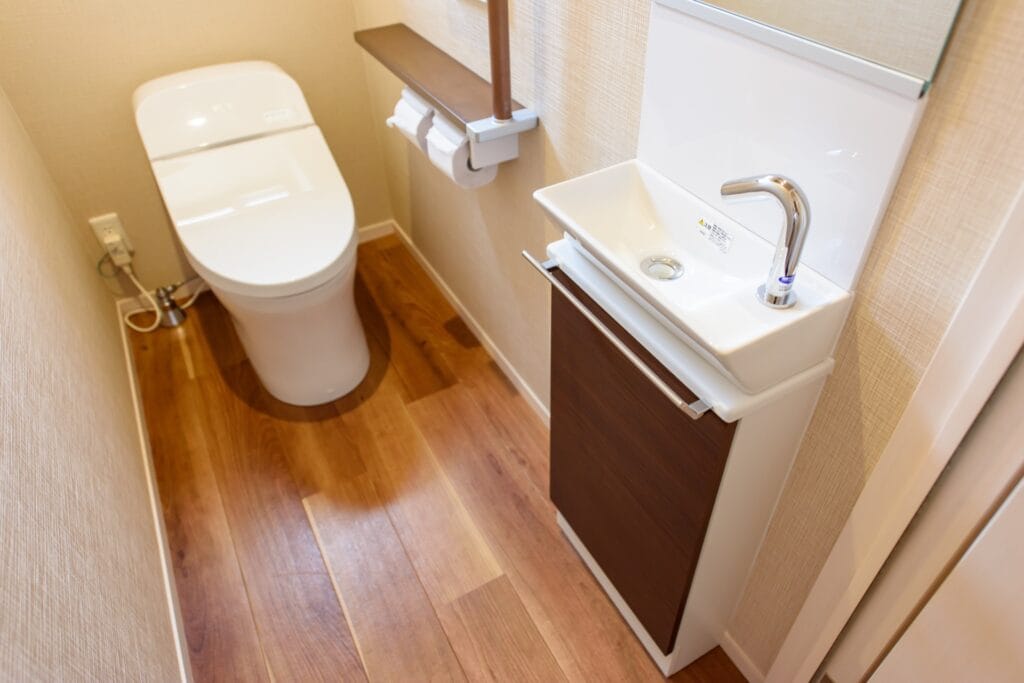 Modern, smal toilet met houtlook vloertegels, een wit toilet en een kleine wastafel met chromen kraan.