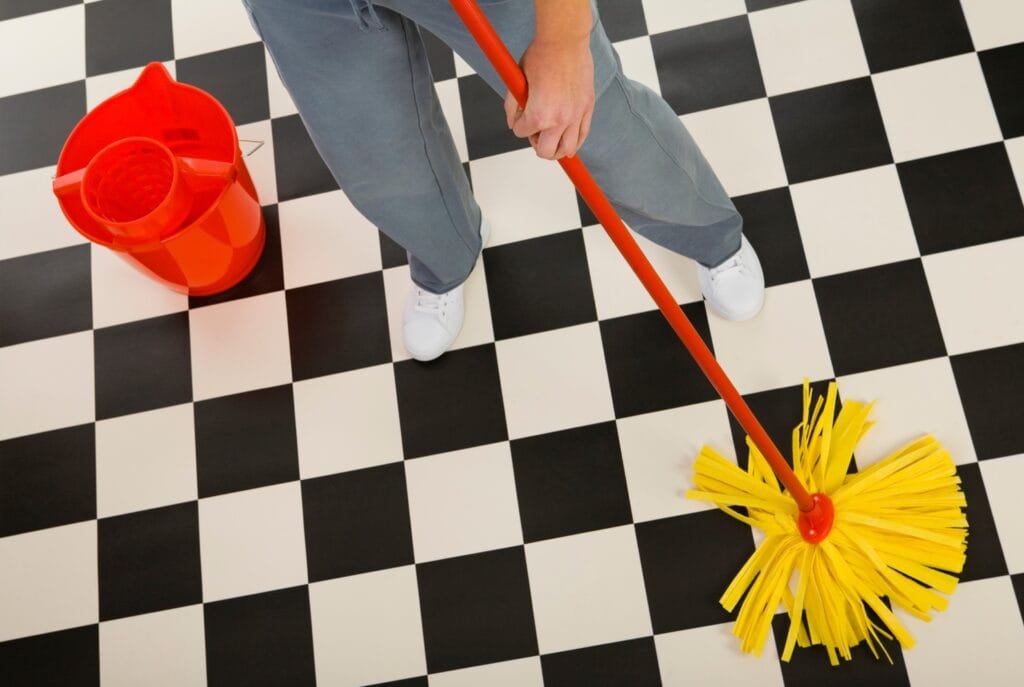 Vloer reinigen met een dweil op zwart-witte geruite vloertegels in de keuken of badkamer. Schoonmaaktips en onderhoud van keramische vloertegels.