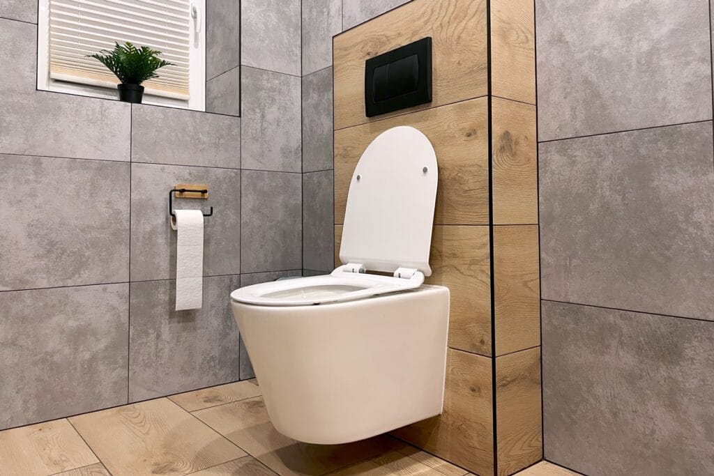 Moderne toiletruimte met grijze wandtegels en houtlook vloertegels, voorzien van een hangend toilet en een klein raam met een plantje op de vensterbank.