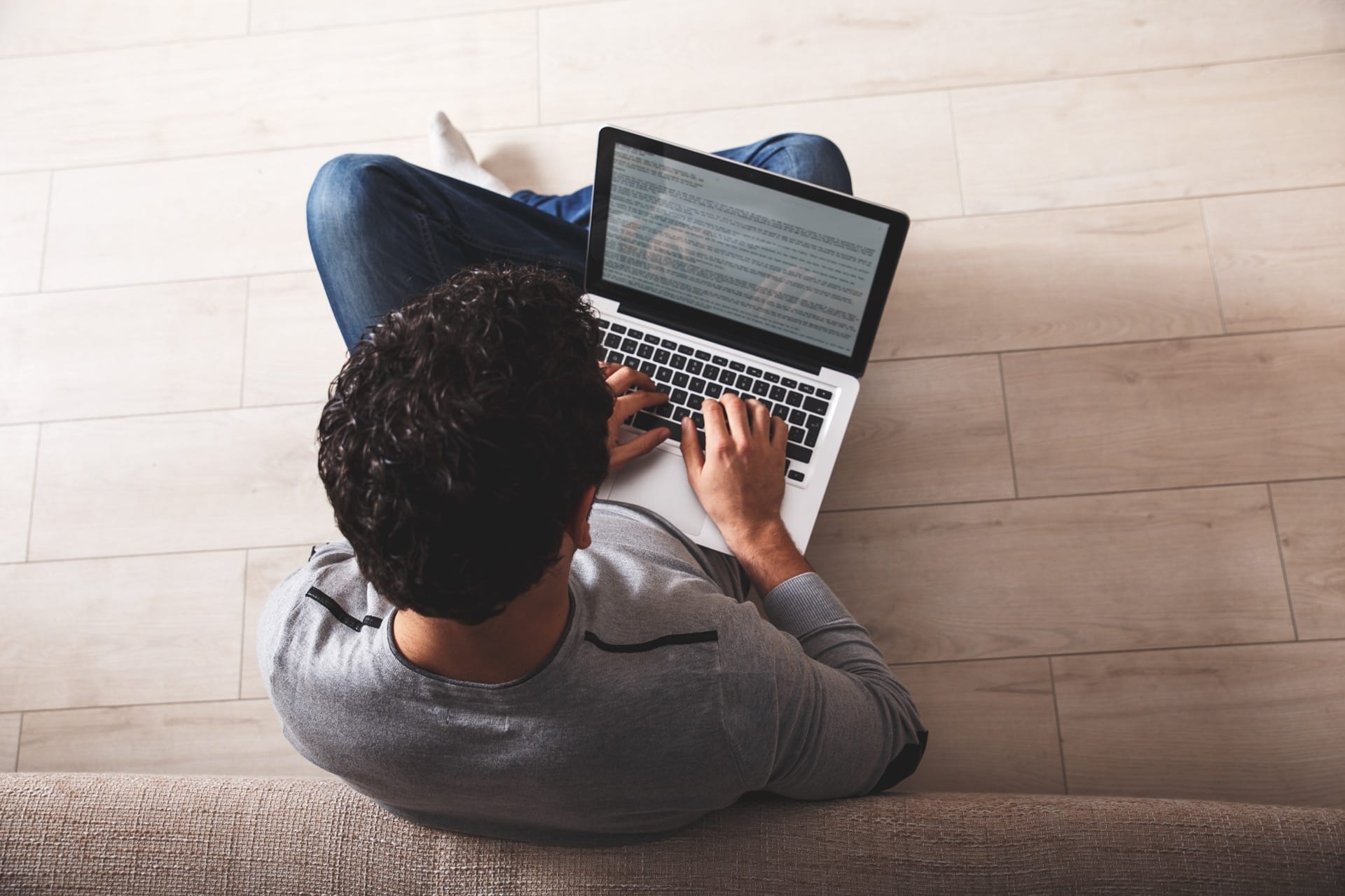 Bovenaanzicht van man met laptop op lichte houtlook vloertegels. Perfect voorbeeld van keramische tegels met houtstructuur in een modern interieur, ideaal voor inspiratie.